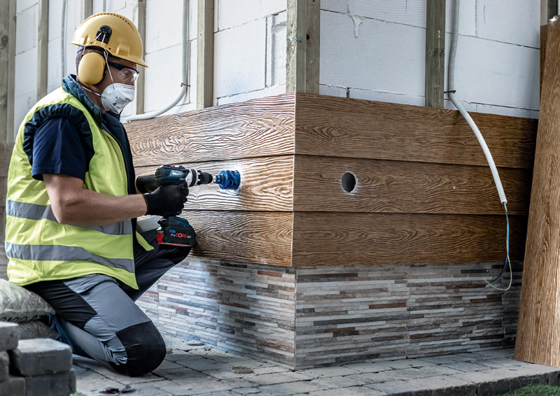 Anwendungsbild, Holzverkleidung, Holzstapel, Baustellenausbildung, Akkuschrauber, Sicherheitsausrüstung